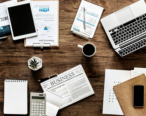 Desk with laptops, notepads, newspapers and cups